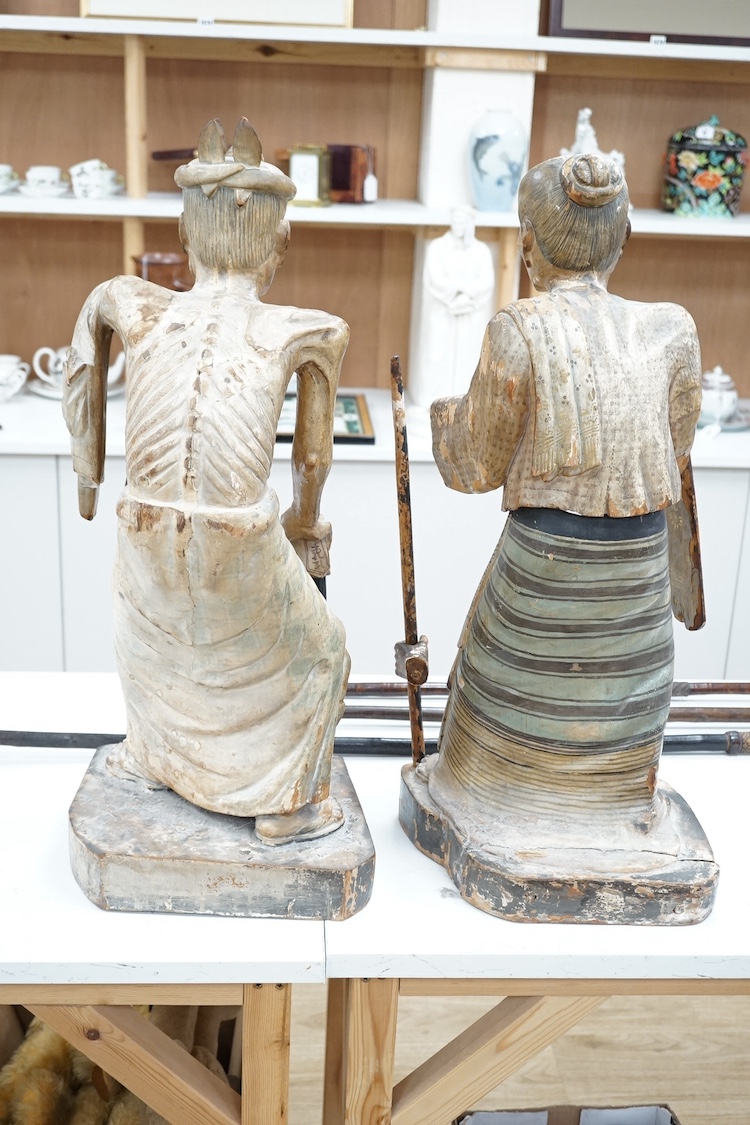 A pair of large Indonesian carved and painted wood figures of an old monk and a lady wearing a sarong, 19th/early 20th century, 70cm. Condition - hand on monk figure broken.